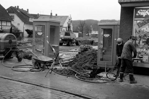 ARH Slg. Weber 02-041/0015, Zwei Arbeiter bauen auf der Zufahrt zum Postparkplatz Am Markt Telefonzellen auf, Alt-Gehrden, zwischen 1970/1980