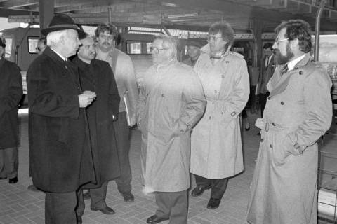 ARH Slg. Weber 02-076/0017, Eine Gruppe von Männern in einem Unterstand mit Fahrzeugen des Dachdeckerbetriebs von Albert Kandelhardt (Mitte, heller Mantel), rechts dahinter Architekt Werner Haller, Gehrden, zwischen 1980/1990