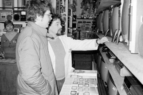 ARH Slg. Weber 02-092/0004, Gilbert Wolf mit Gundi Wolf (links) bei einer Beratung über Fernsehgeräte in seinem Fachgeschäft für Unterhaltungselektronik in der Dammstraße, Gehrden, zwischen 1980/1990