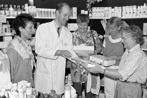 ARH Slg. Weber 02-093/0001, Mehrere Frauen erhalten in einer Apotheke Geschenke von einem Apotheker, zwischen 1980/1990