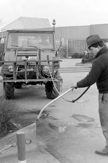 ARH Slg. Weber 02-100/0002, Ein Mann reinigt einen Gehweg, im Hintergrund das Hallenfreibad der Stadt Gehrden, zwischen 1980/1990