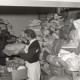 Archiv der Region Hannover, ARH NL Koberg 9266, Zwei Frauen tauschen ein Paket aus, rundherum Stapel von Kleidung, Decken und Kinderspielzeug, möglichweise in einer Kleiderausgabestelle?, Hannover