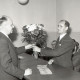 ARH NL Koberg 9373, Zwei Männer in Anzügen tauschen einen Blumenstrauß über einem Tisch mit Geldscheinen aus, mehrere Männer im Hintergrund?, Hannover