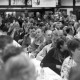 ARH NL Mellin 01-121/0009, Menschen in einem Raum und an Tischen versammelt