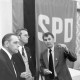 ARH NL Mellin 01-149/0019, Drei Männer in einem Gespräch vor einer Art Wandteppich mit dem Aufdruck "SPD"