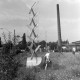 ARH NL Mellin 01-194/0005, Mädchen auf einer Wiese neben einer Statue(?), im Hintergrund ein Fabrikschornstein