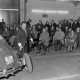 Archiv der Region Hannover, ARH NL Mellin 02-173/0010, Mann beim Radwechsel an einem Auto vor einem Publikum