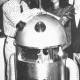 Stadtarchiv Neustadt a. Rbge., ARH Slg. Bartling 661, Mann und Frau stellen einen Roboter im Werbeeinsatz in einem Bekleidungsgeschäft vor