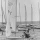 Stadtarchiv Neustadt a. Rbge., ARH Slg. Bartling 1092, Mit drei Mann besetztes Jeton-Boot in voller Fahrt vorm Wind vorbei an einem Anleger mit Booten, Steinhuder Meer