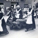 Stadtarchiv Neustadt a. Rbge., ARH Slg. Bartling 1309, Gruppe von Frauen mit "historischen" Schürzen beim Ernteumzug, in ihrer Mitte eine Karre mit Erntefrüchten, im Hintergrund ein EDEKA-Laden, Mandelsloh