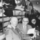 ARH Slg. Bartling 2097, Zwei ältere Männer mit anderen Zuschauern sitzend auf der Tribüne einer Turnhalle, Blick von rechts auf die erste Reihe