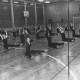 Stadtarchiv Neustadt a. Rbge., ARH Slg. Bartling 2124, Gymnastik-Übung von Frauen, die in Sportleggings auf dem Boden einer Halle (mit Glasbausteinwand) sitzen, die Arme nach oben streckend, Neustadt a. Rbge.