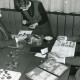 Stadtarchiv Neustadt a. Rbge., ARH Slg. Bartling 2251, Zwei Numismatiker und zwei Philatelisten sich gegenüber sitzend am Tisch sowie eine Dame stehend bei der Prüfung einer Münze mit Lupe, Neustadt a. Rbge.
