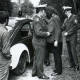 Stadtarchiv Neustadt a. Rbge., ARH Slg. Bartling 3425, Durchsuchung eines festgenommenen Mannes durch einen Polizisten mit gezogener Pistole neben einem auf einem Waldweg stehenden Streifenwagen (VW-Käfer), Bordenau