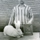 ARH Slg. Bartling 3614, Präsentation eines auf dem Tisch sitzenden weißen Angorakaninchens durch den hinter dem Tisch stehenden Züchter N. N., neben dem Kaninchen der Preis des Bundes-Siegers 1987 (Stuttgart Killesberg) des ZDK, Neustadt a. Rbge.