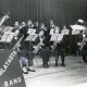 Stadtarchiv Neustadt a. Rbge., ARH Slg. Bartling 3941, Auftritt der "Blatasta-Band", einer Blaskapelle mit lauter jungen Männern, unter der Leitung von N. N. auf einer Bühne mit Vorhang, Bordenau