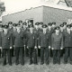 Stadtarchiv Neustadt a. Rbge., ARH Slg. Bartling 4143, Gruppenfoto der Feuerwehrleute in Ausgehuniform auf dem Rasen hinter dem Gebäude, Empede