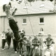 Stadtarchiv Neustadt a. Rbge., ARH Slg. Bartling 4199, Versuch eines Kindes, vor Zuschauern auf einer Strickleiter am Ast eines Baumes hängende Preise zu holen beim Kinderfest, Hagen