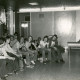 Stadtarchiv Neustadt a. Rbge., ARH Slg. Bartling 4575, Jugendliche im DRK-Heim unter Wimpeln in einer Reihe sitzend in Diskussion mit einem Mann, der am Tisch sitzt, Mardorf