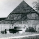 Stadtarchiv Neustadt a. Rbge., ARH Slg. Bartling 4672, Bauernhaus, Fachwerkbau mit Krüppelwalmdach, mit Ziegeln gedeckt, Giebelansicht, vor dem Bretterzaun an der Straße ein Sitzplatz aus Mühlensteinen mit der Jahreszahl 1974, Niedernstöcken