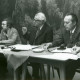 Stadtarchiv Neustadt a. Rbge., ARH Slg. Bartling 4762, Fünf Männer in einem Saal hinter einem Tisch vor Waldtapete sitzend, Otternhagen