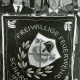 Stadtarchiv Neustadt a. Rbge., ARH Slg. Bartling 4916, Präsentation des Fahnentuchs der Freiwilligen Feuerwehr von 1954 durch zwei dahinter stehende Feuwehrmänner, Scharrel