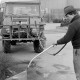 Archiv der Region Hannover, ARH Slg. Weber 02-100/0002, Ein Mann reinigt einen Gehweg, im Hintergrund das Hallenfreibad der Stadt Gehrden